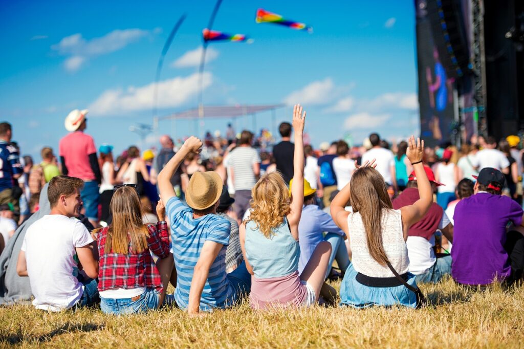 Group of teenagers at summer music festival, sitting on the grass in front of stage