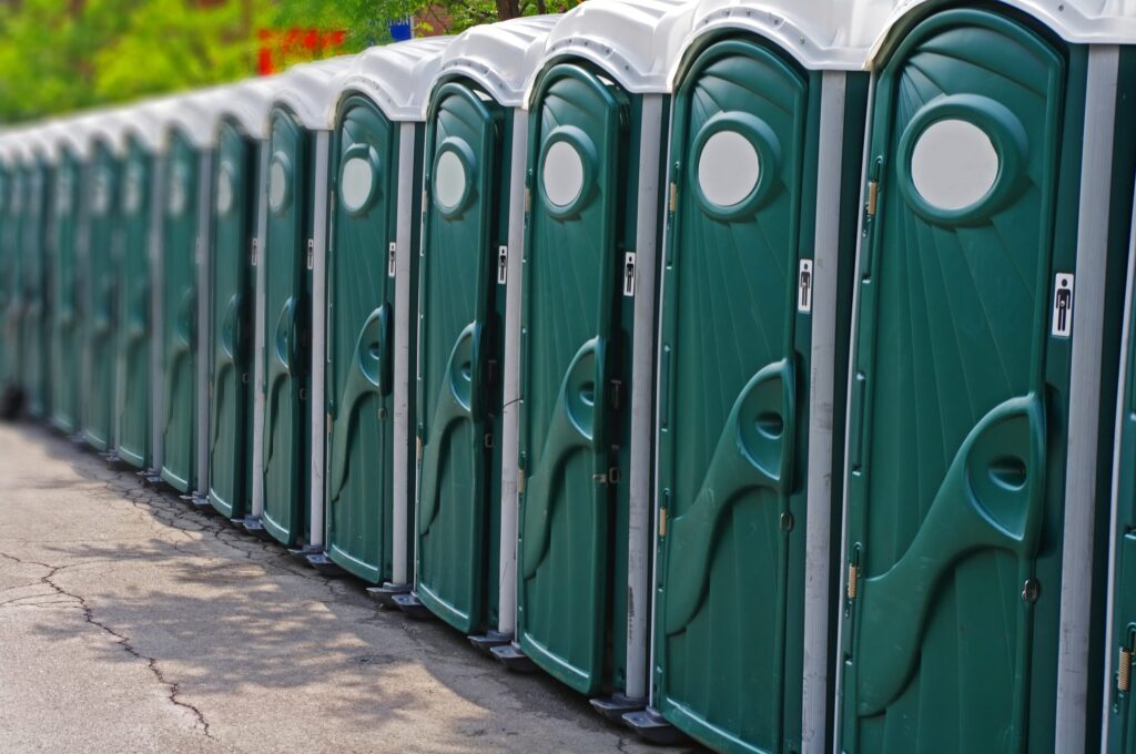 a row of green porta potties are lined up outside of a huge construction project