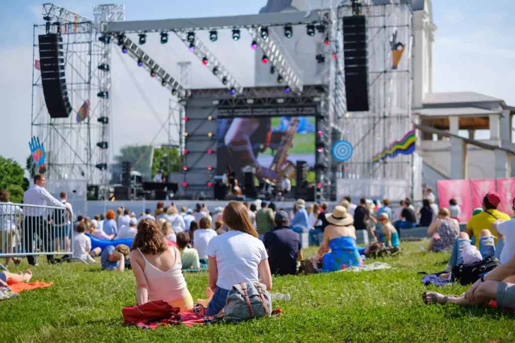 A group of people sitting around a large stage during an outdoor music festival
